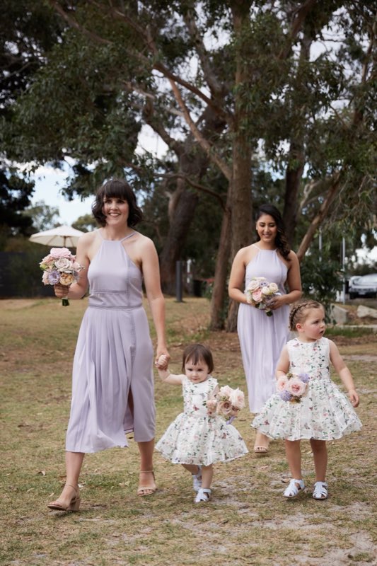 Flower girls and bridesmaids in lilac walking together holding small posies