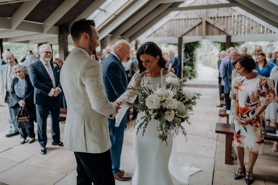 Couple exchanging vows under a timber pavilion, bride holding a full white bouquet